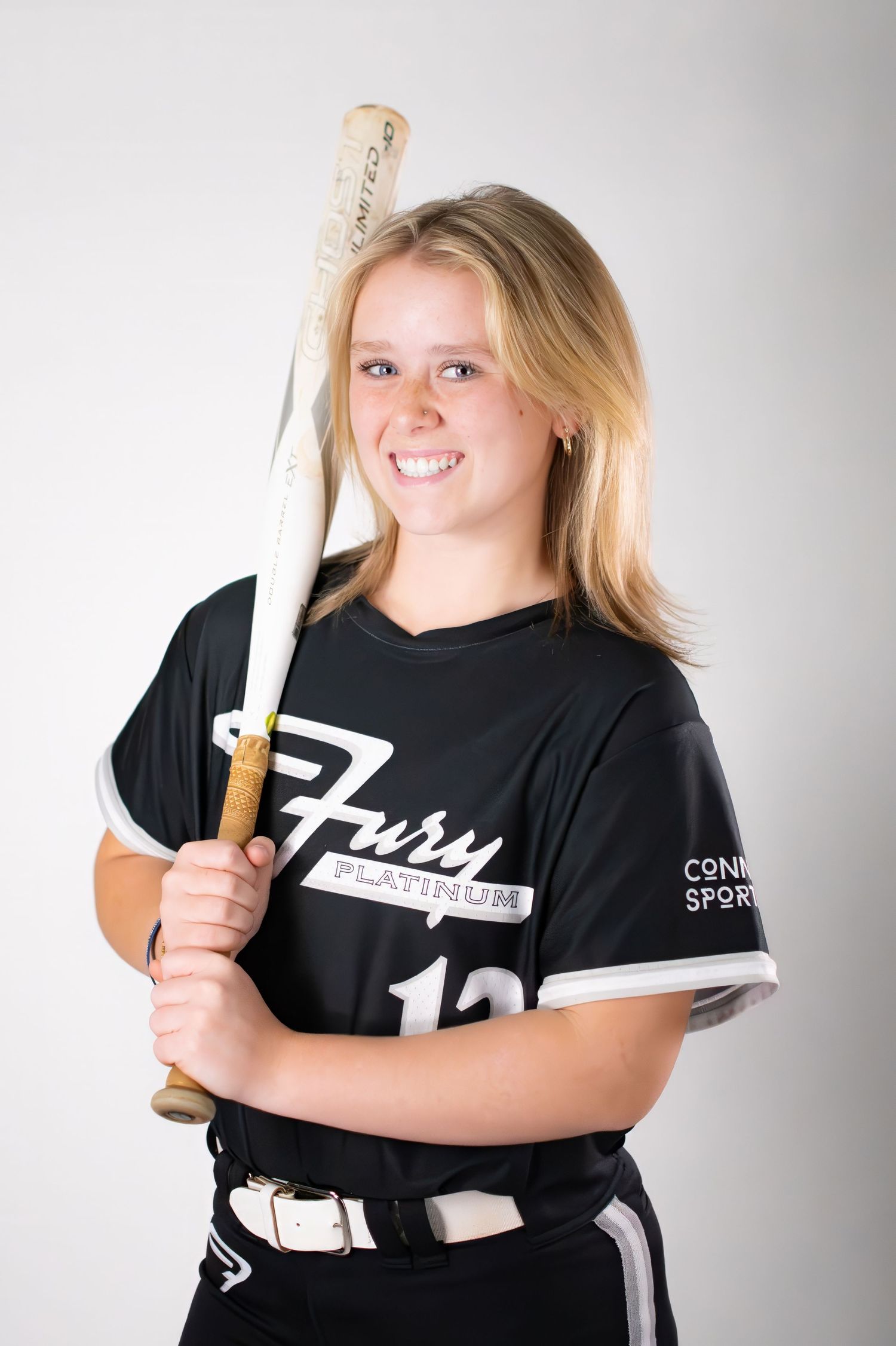 Smiling blonde female softball player #12 in black Fury Platinum jersey holding bat.