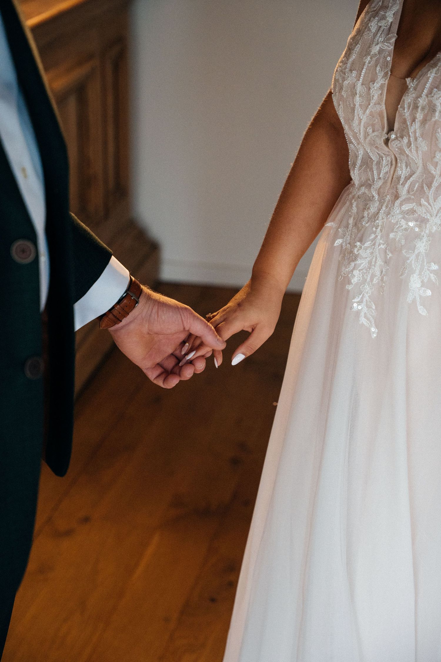 Close-up of bride and groom holding hands, showcasing lace wedding dress and dark suit.
