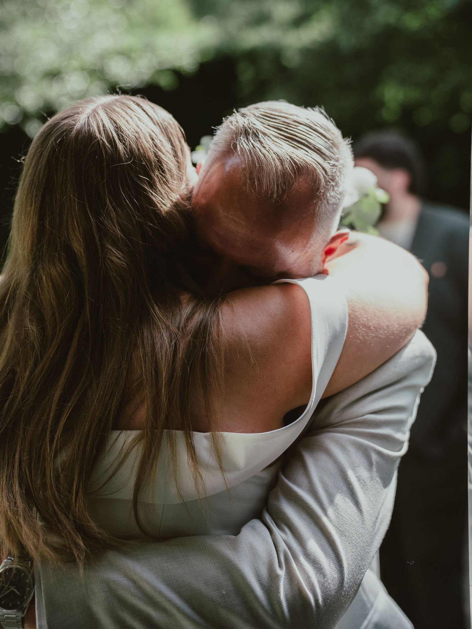 Bride and groom share a tender embrace surrounded by lush green foliage at outdoor wedding.