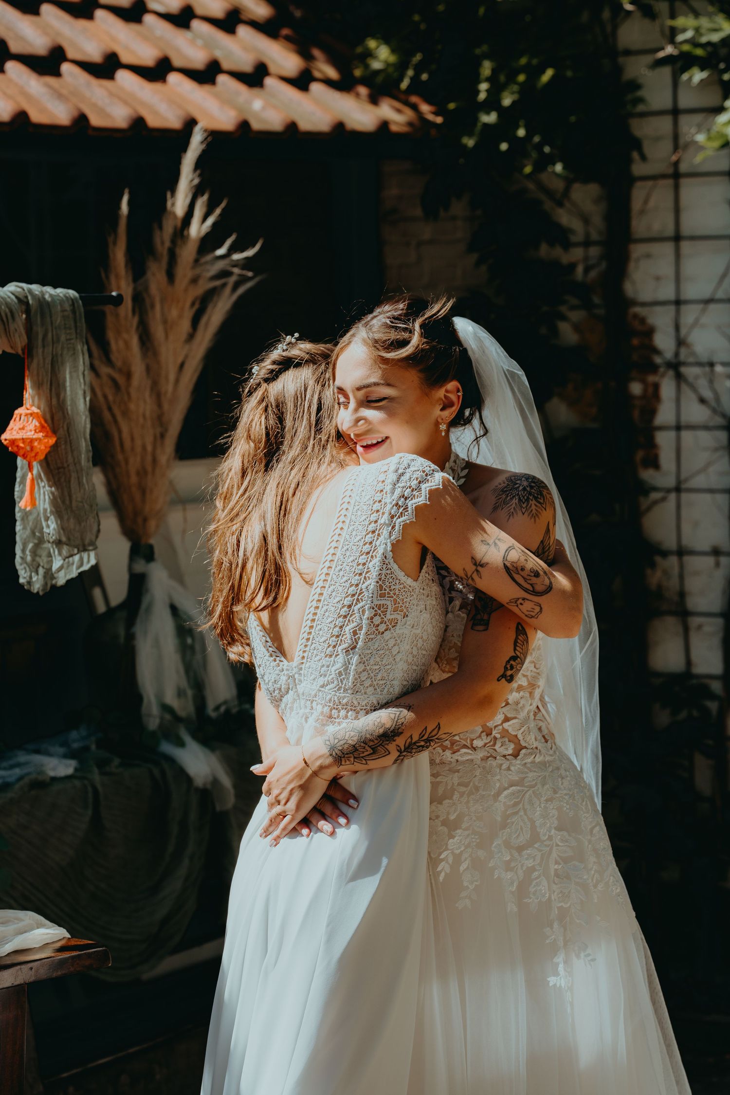 Two brides in white lace wedding dresses sharing a warm embrace at their outdoor wedding celebration.