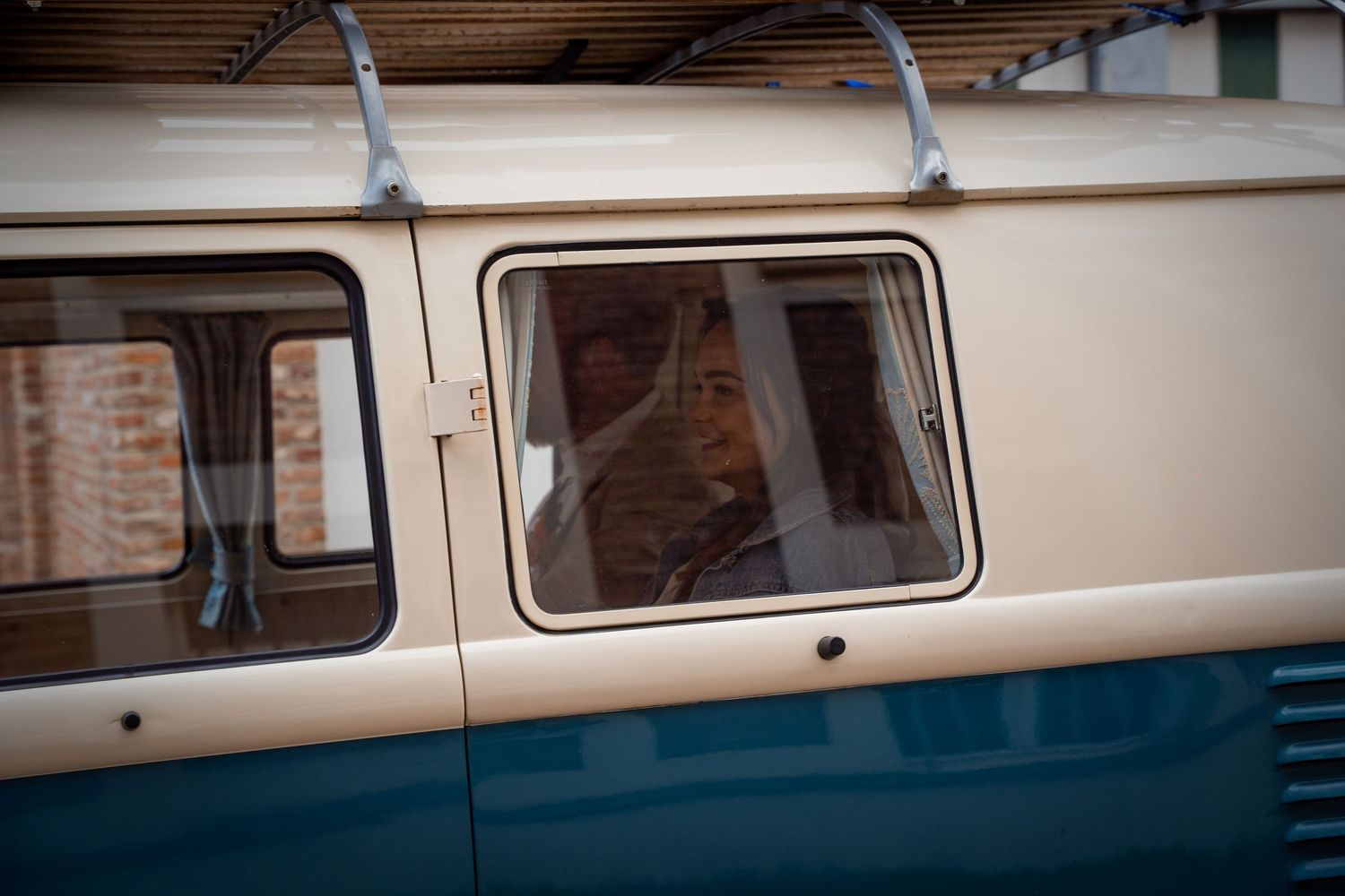 A person sitting inside a vintage blue and cream Volkswagen van, visible through the side window.