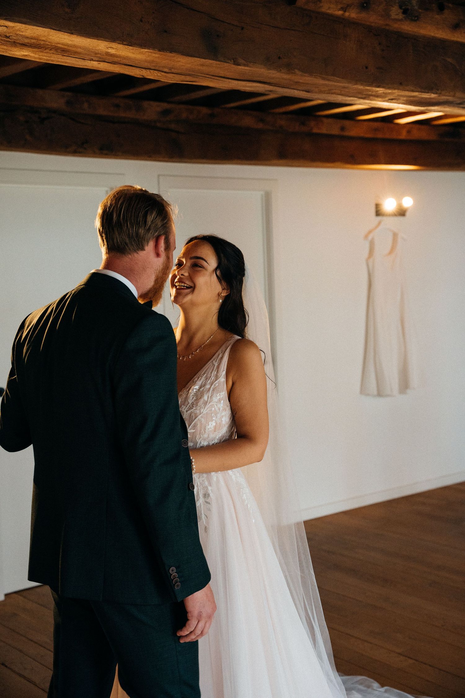 Smiling bride in lace gown shares a tender moment with groom in rustic wooden interior.