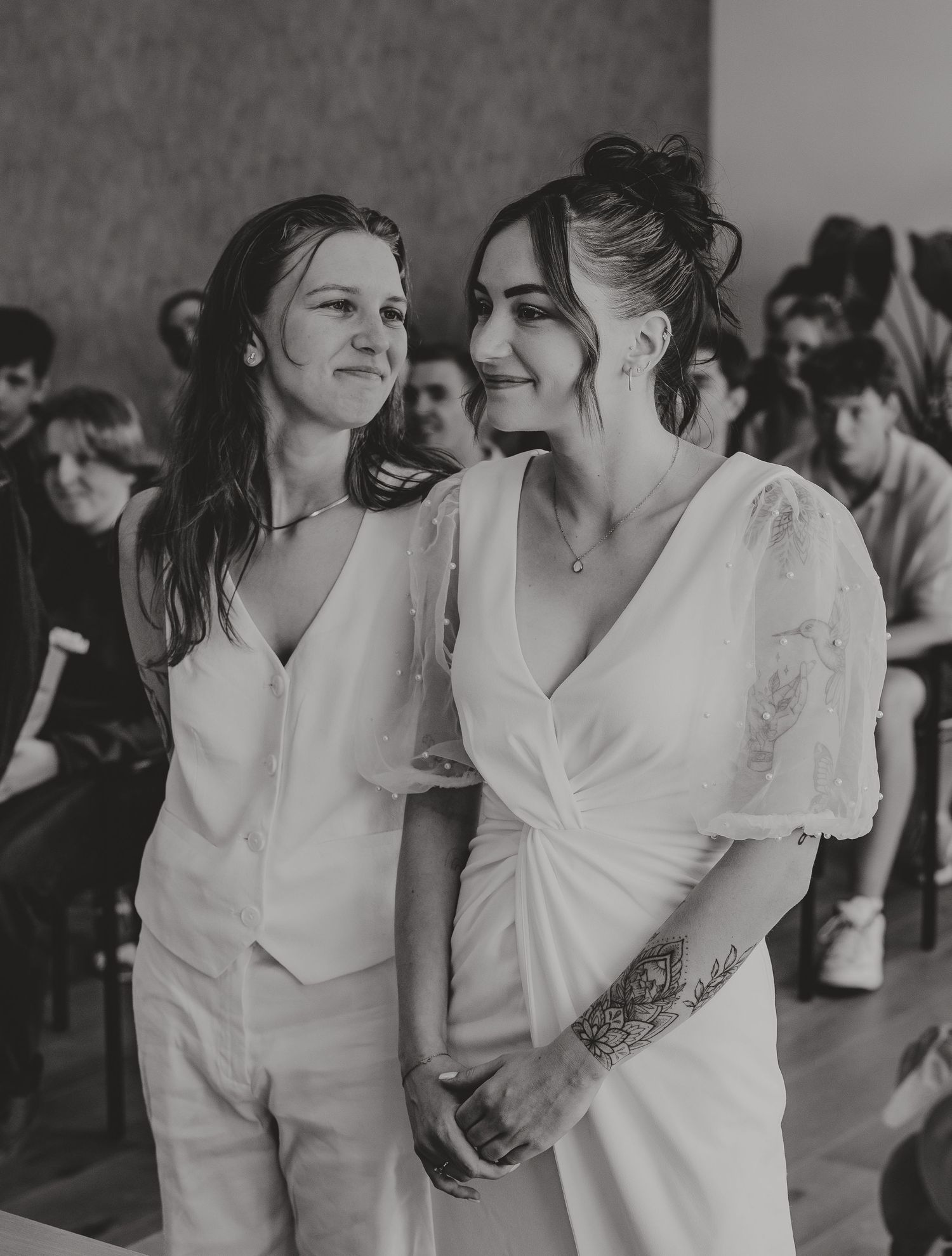 Two brides in white wedding attire standing together during their wedding ceremony in black and white photo.