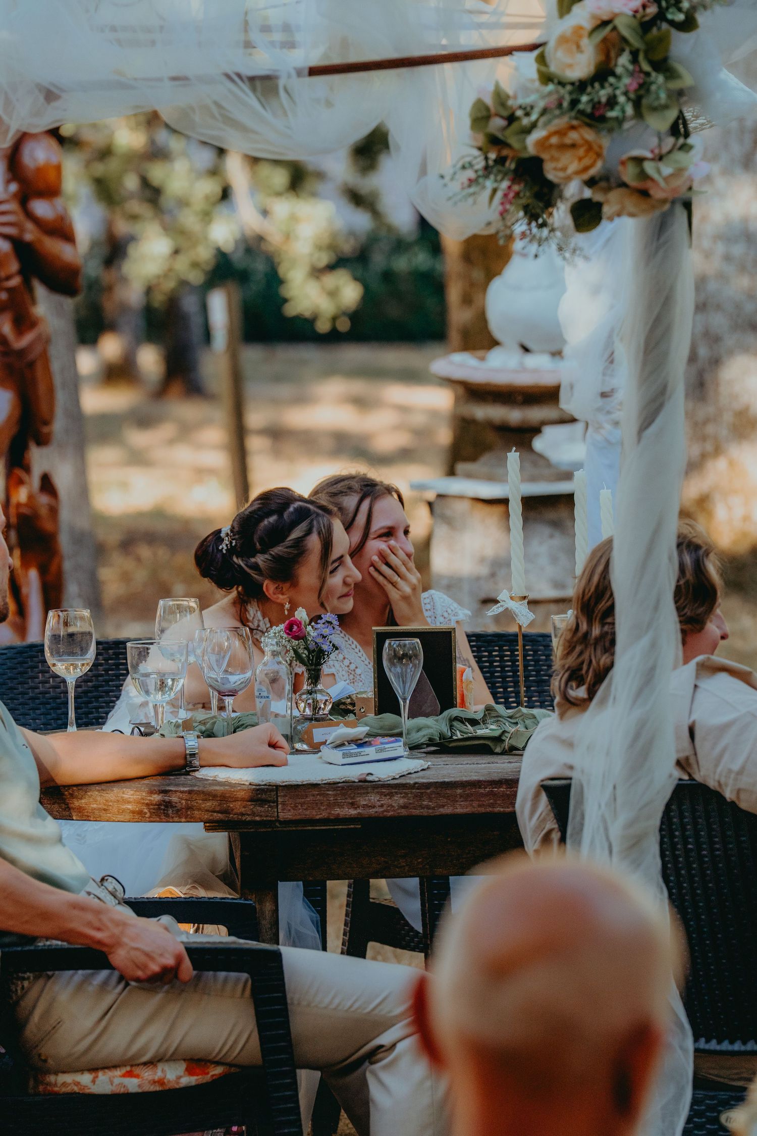 Two brides laughing and sharing an intimate moment together at their outdoor wedding reception dinner.