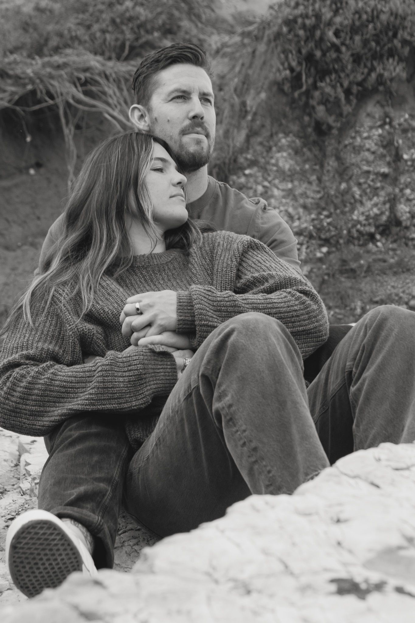 Black and white photo of couple sitting on rocks outdoors, woman leaning back on man.