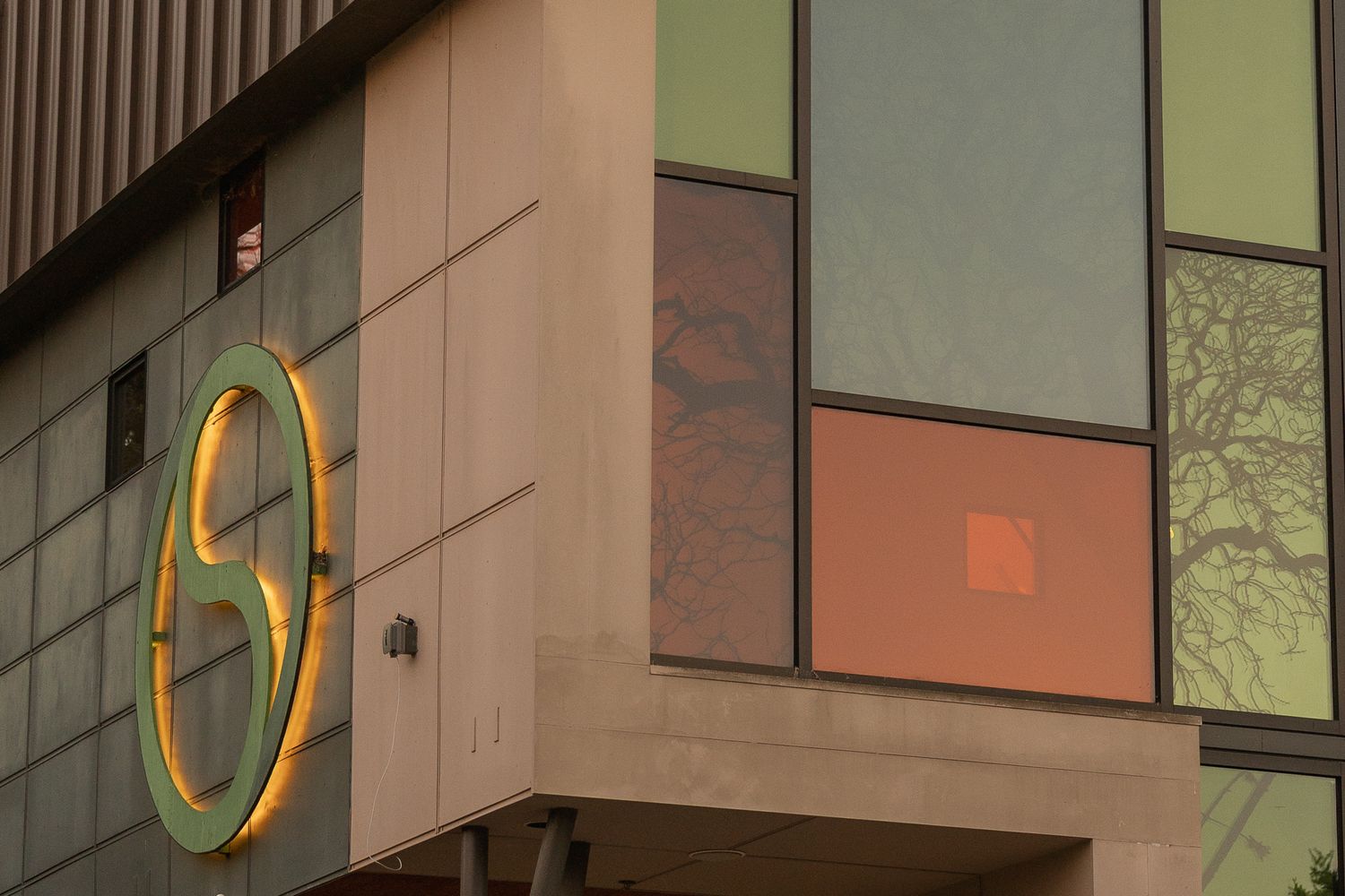 Modern building exterior with colorful glass panels and a circular green and yellow logo sign at dusk.