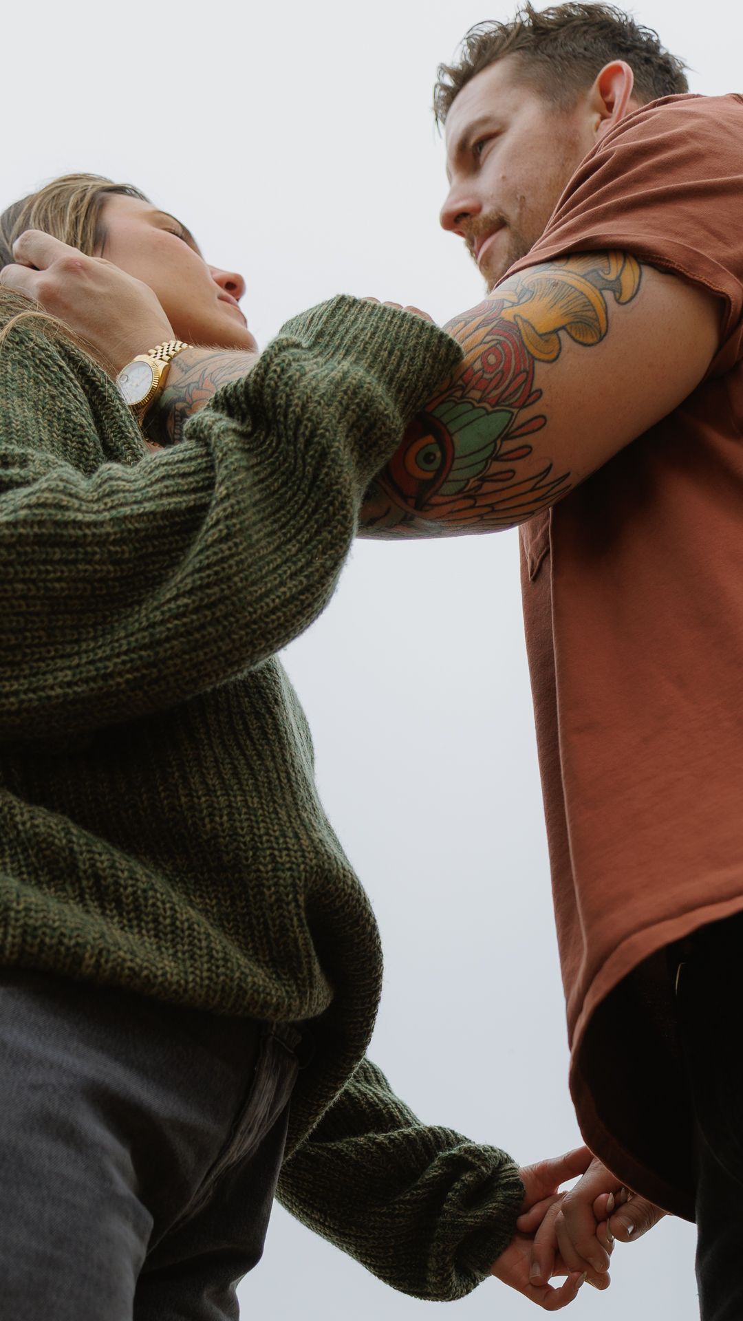 A couple holds hands and gazes at each other, the man displaying a vibrant sleeve tattoo.
