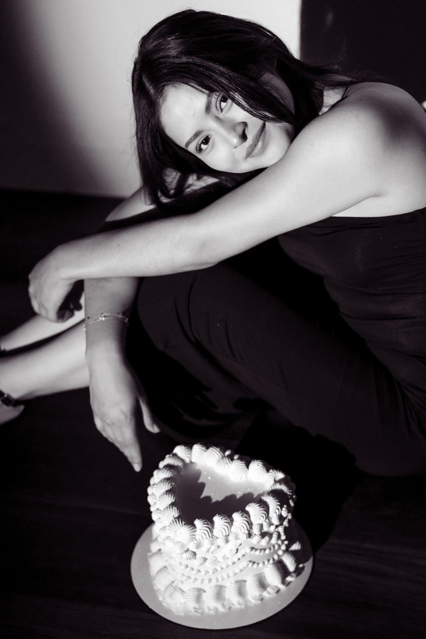 Black and white photo of a woman sitting on floor beside a decorated white cake.