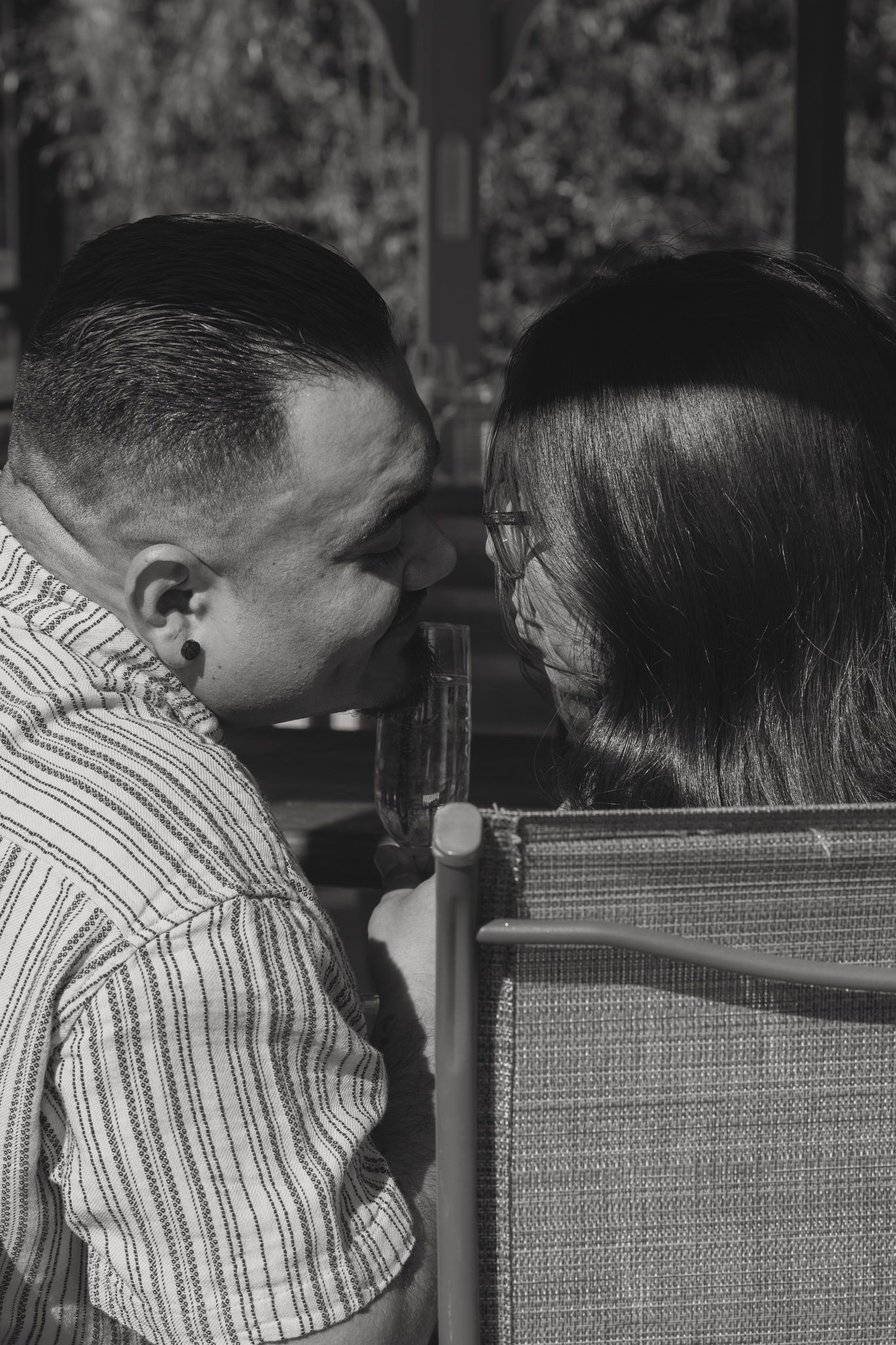 Black and white photo of a couple leaning close together, about to kiss, seated outdoors in chairs.