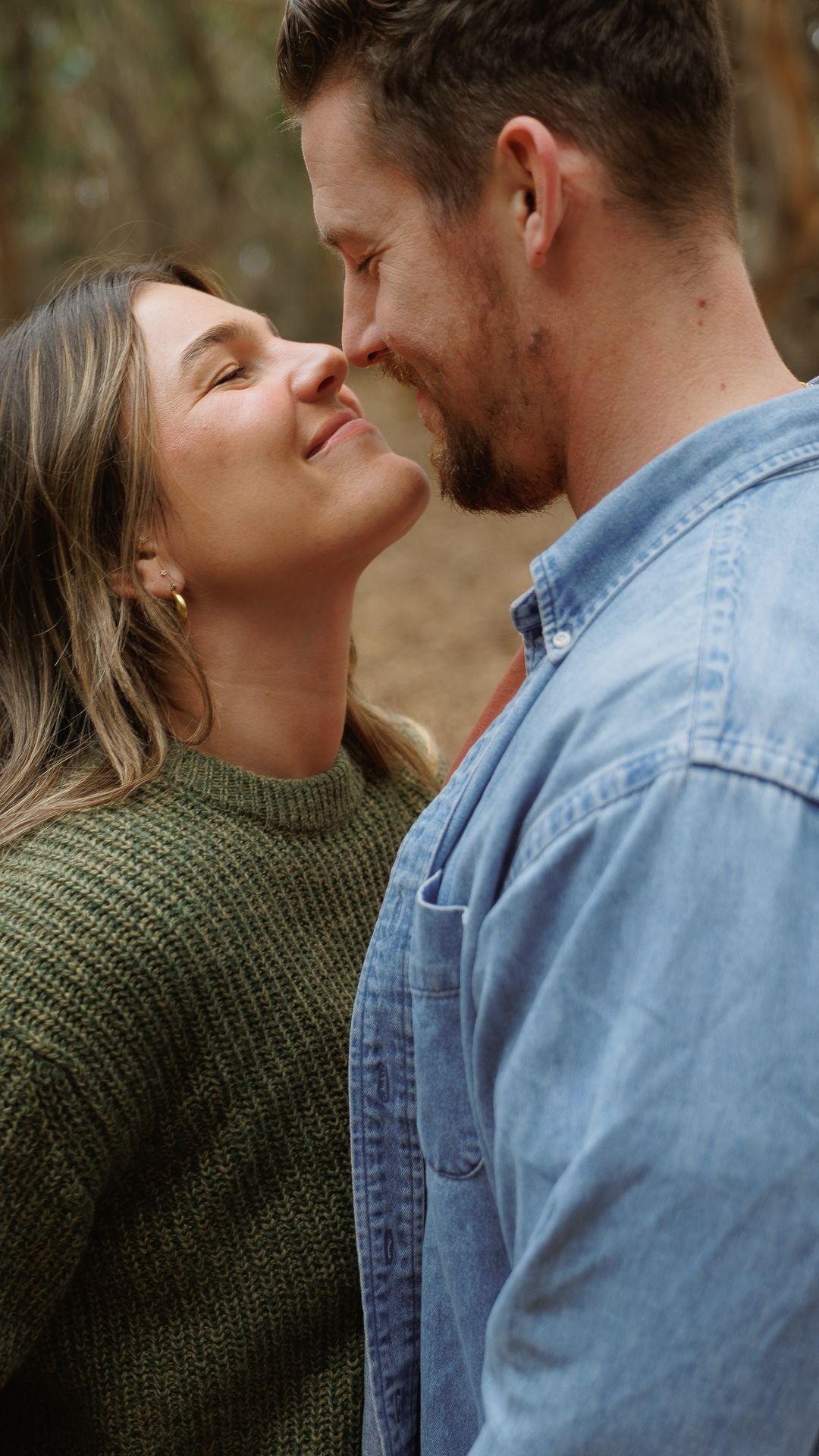 A close-up of a couple sharing a tender nose-to-nose moment, smiling softly outdoors.