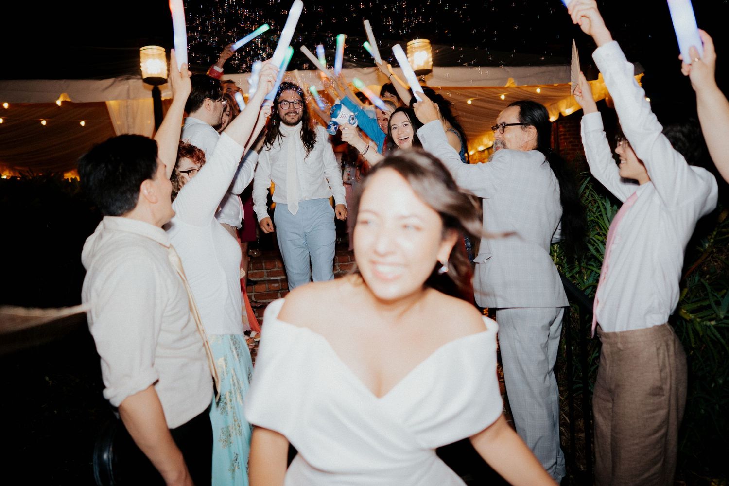 Wedding guests dance and celebrate with raised arms at a nighttime outdoor reception.