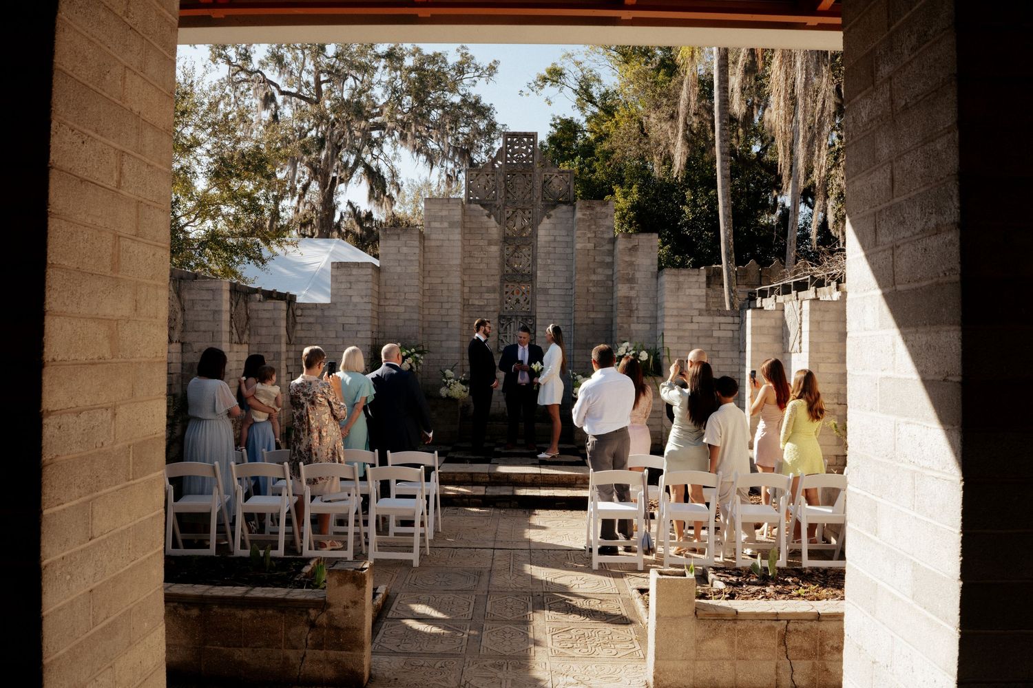Outdoor wedding venue setup with white chairs arranged in rows against stone architecture.