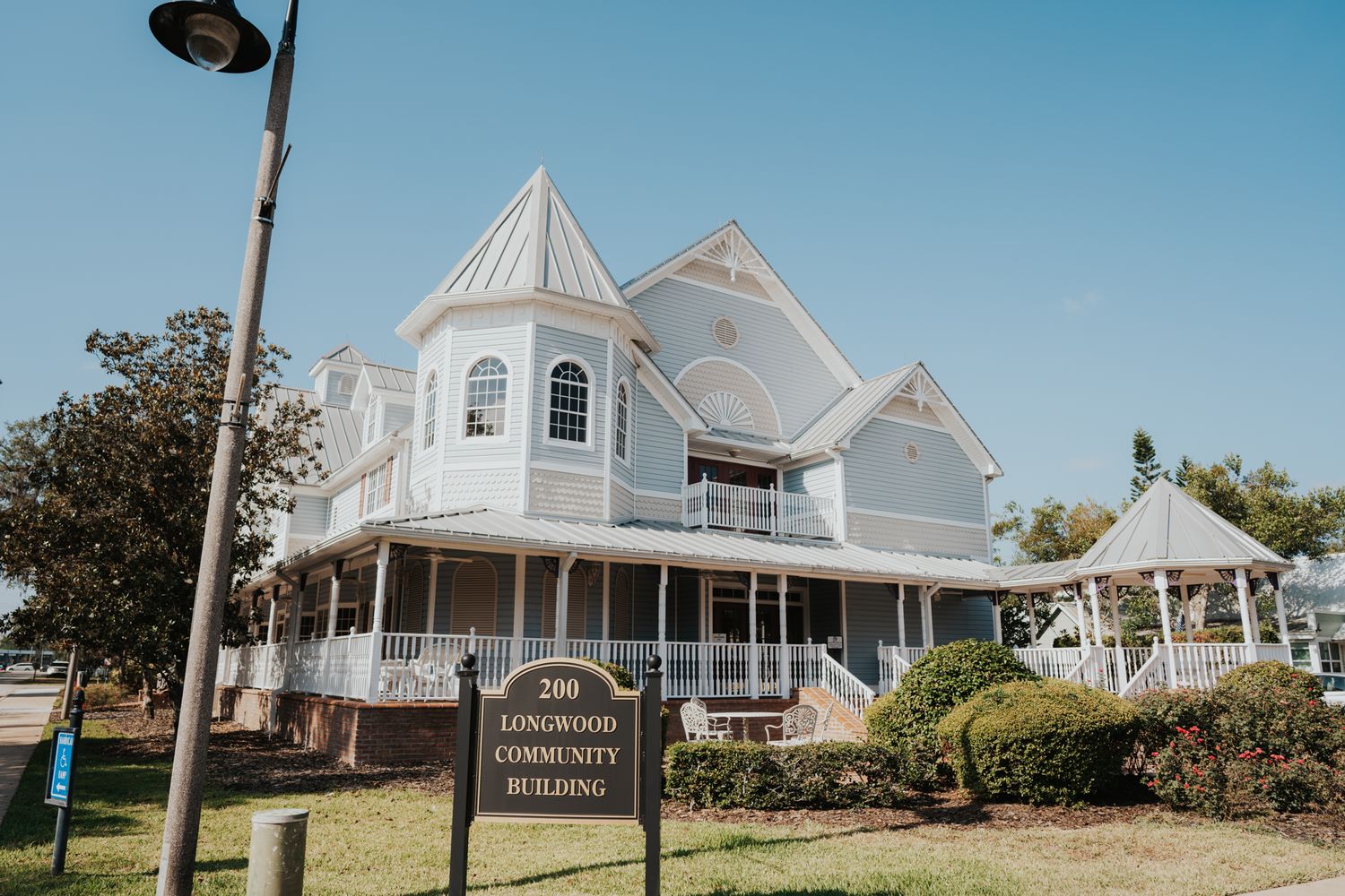 Victorian-style white mansion with wraparound porch and turret against blue sky.