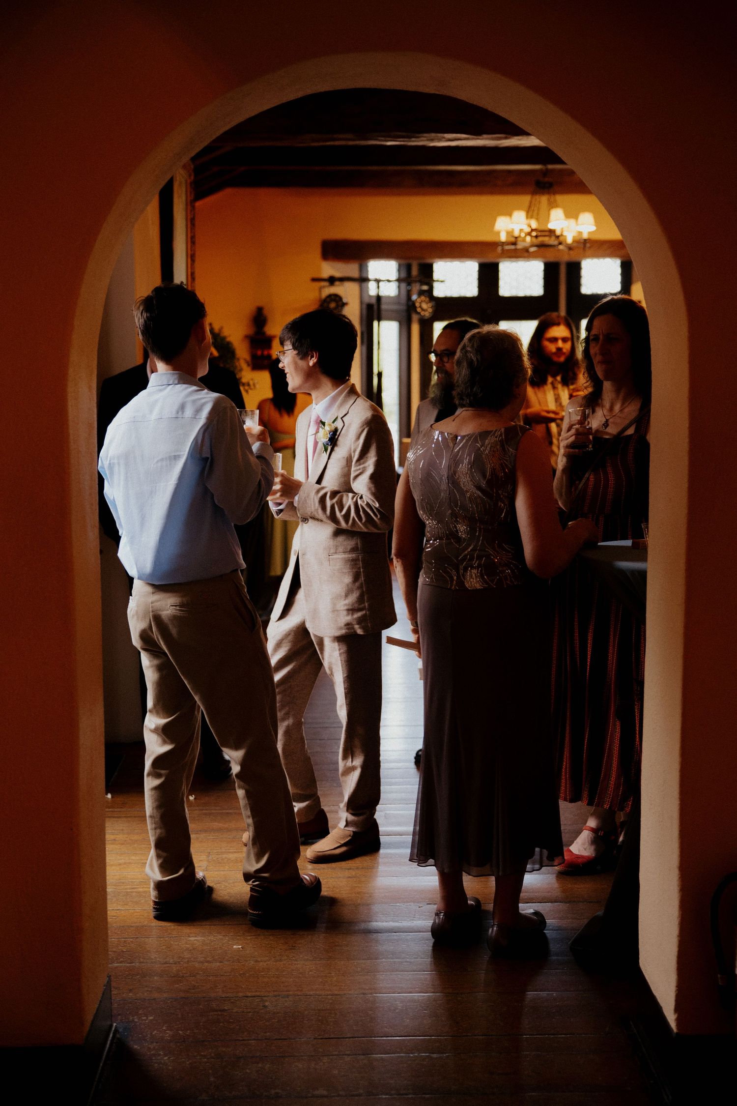 Silhouettes of wedding guests gather in a dimly lit room with arched doorways and warm ambient lighting.