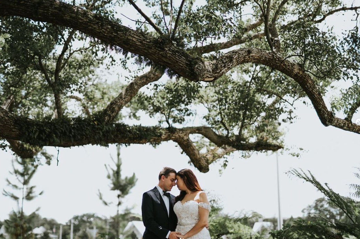 A romantic wedding couple embraces beneath a sprawling oak tree draped with Spanish moss.