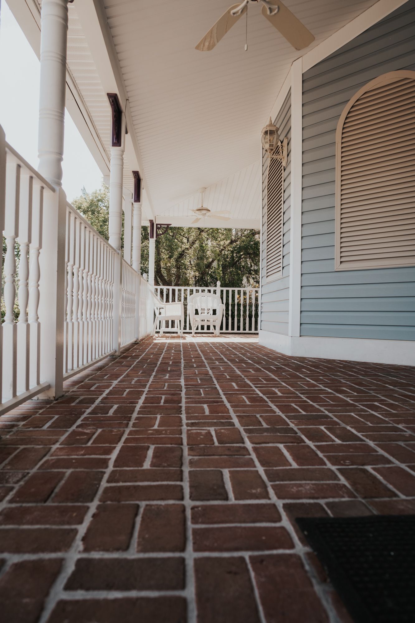 Brick-floored porch with white railings and rocking chairs overlooking garden.