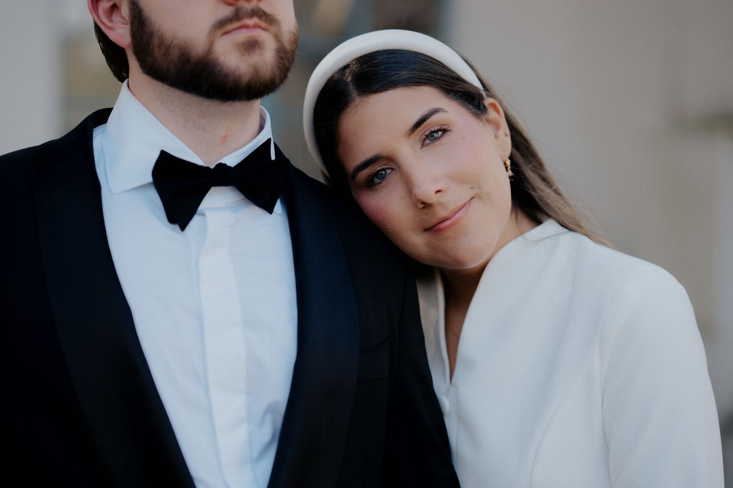 Close-up portrait of newlyweds in black and white formal attire against neutral background.