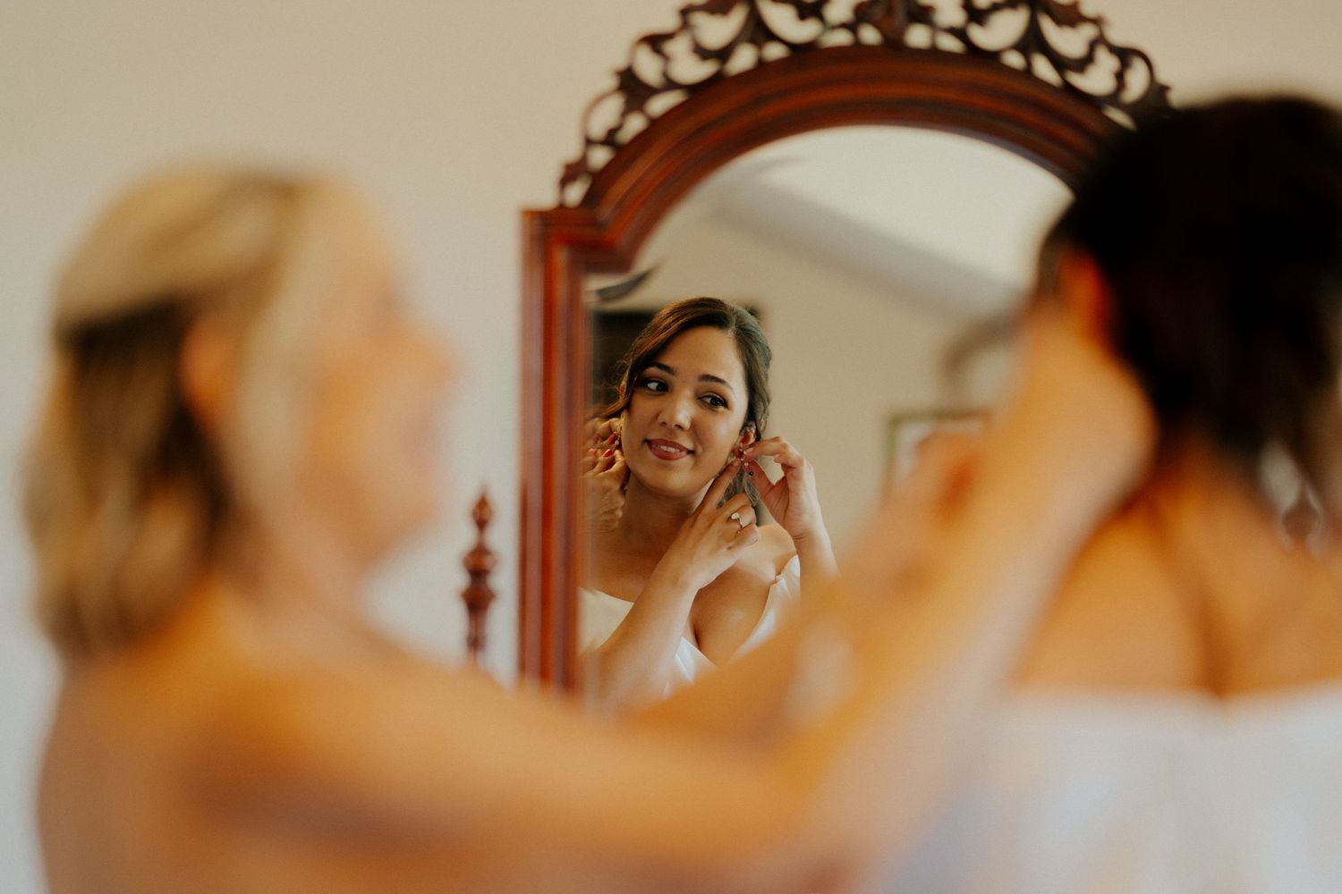 A reflection in an ornate wooden mirror shows a joyful getting-ready moment during wedding preparations.