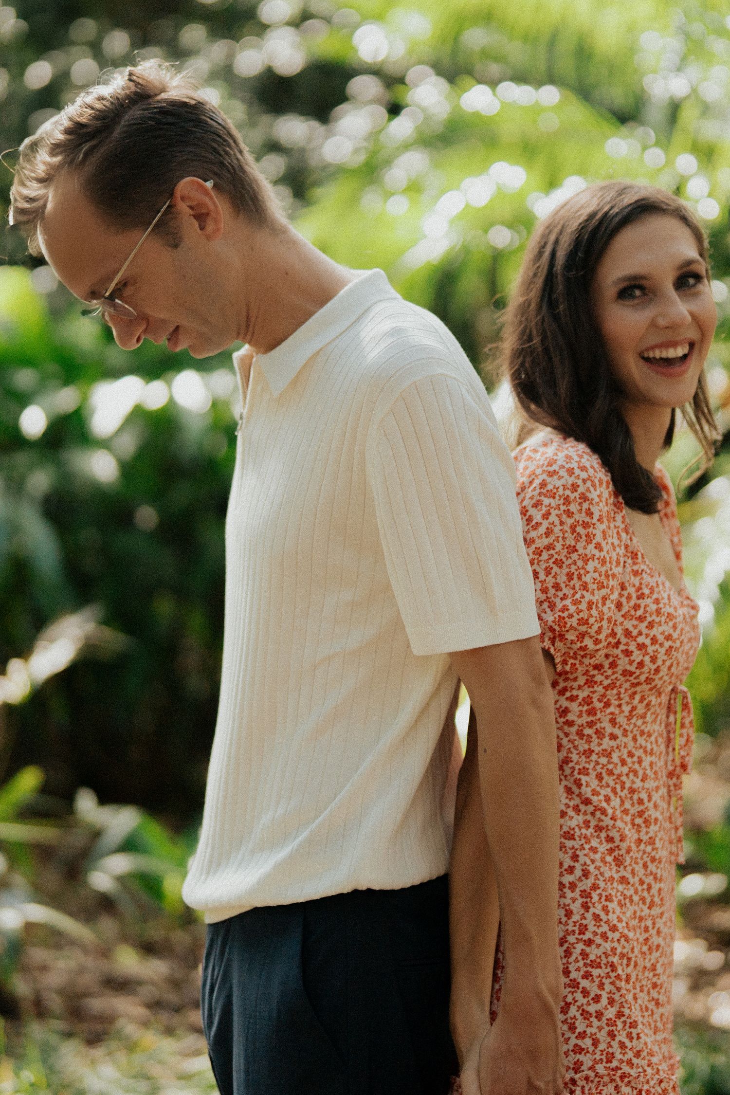 A couple shares a joyful moment outdoors, with the woman wearing a red polka dot dress and the man in a white shirt.