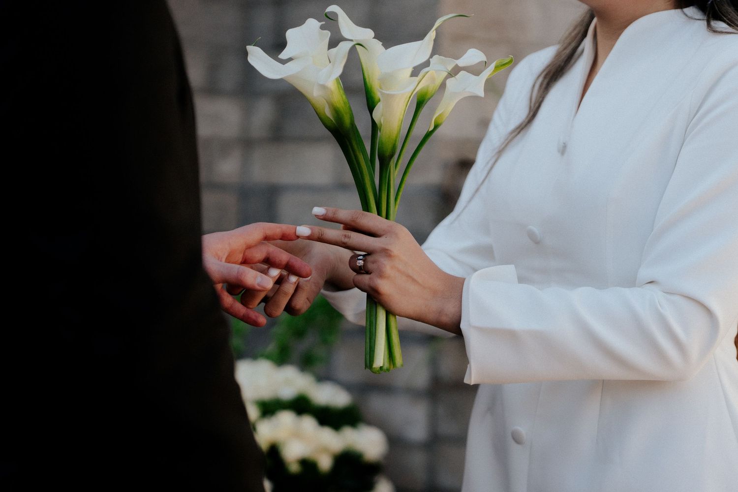Bride holding white calla lily bouquet during wedding ring exchange ceremony.
