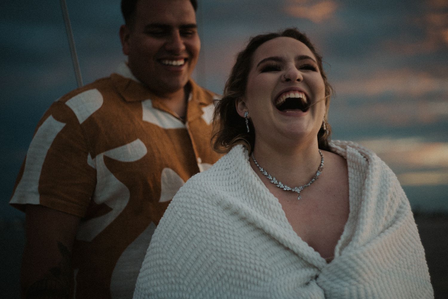 A couple sharing a joyful moment at sunset on a boat, with one wearing a cozy white sweater.