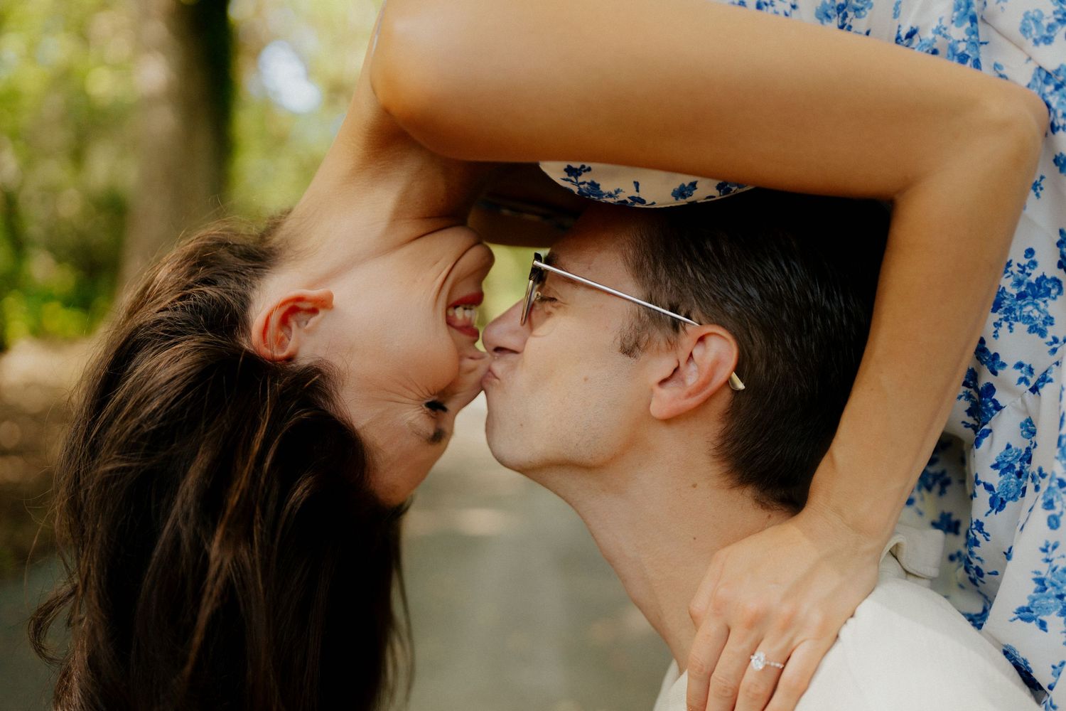 Close-up of smiling couple nearly kissing outdoors in soft natural light with blurred greenery background.