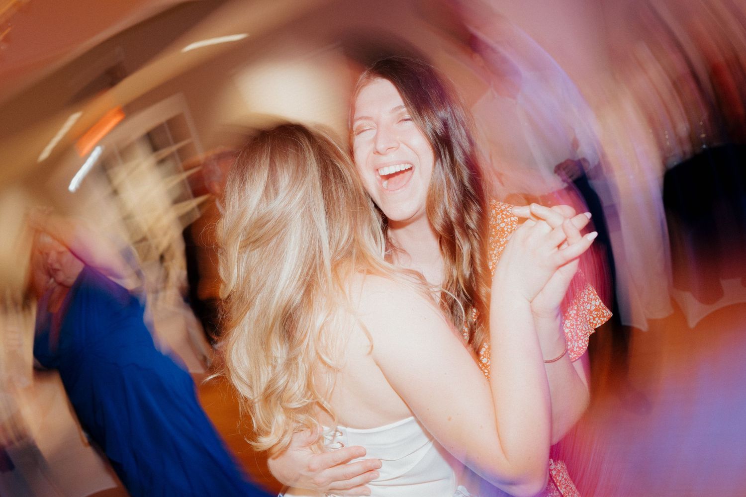 Two women laughing and dancing together at a lively wedding reception party.