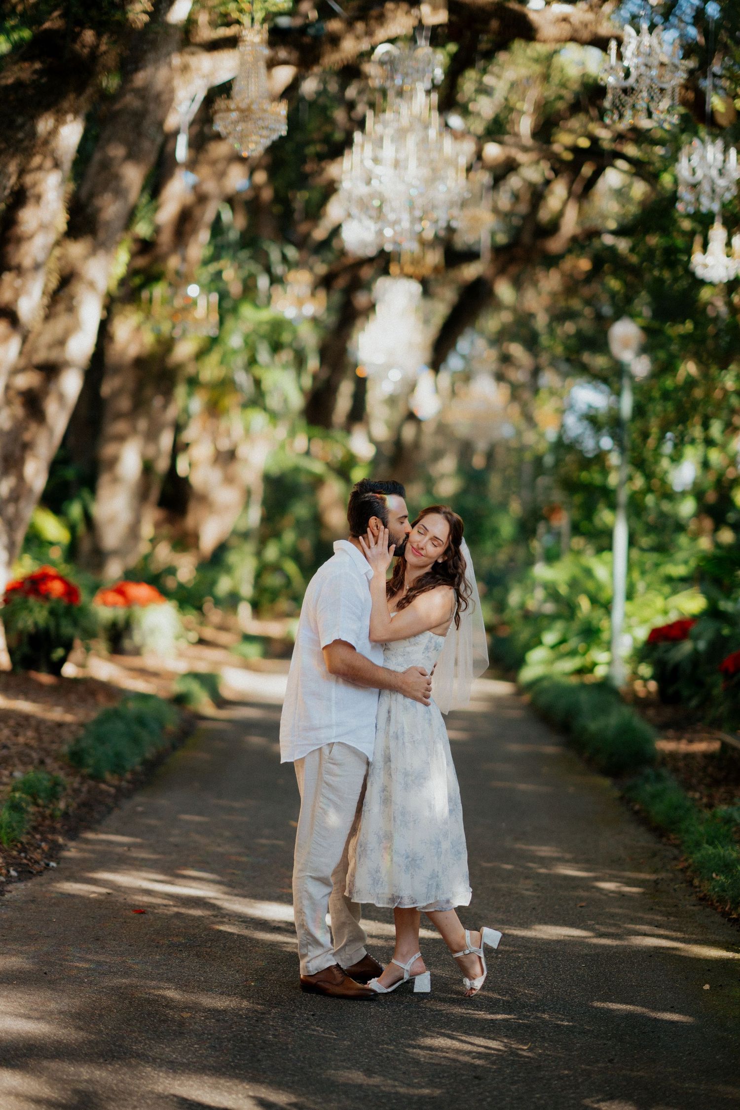 A couple shares intimate moments along a tree-lined path with Spanish moss hanging overhead.
