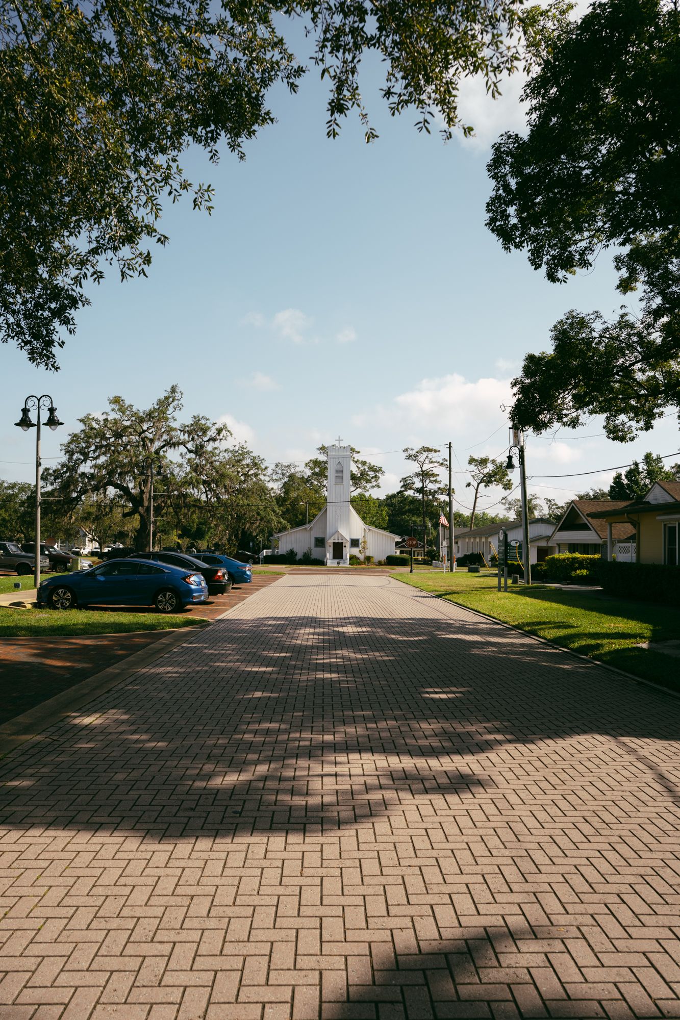Brick paved street leading to white church with trees lining the path.
