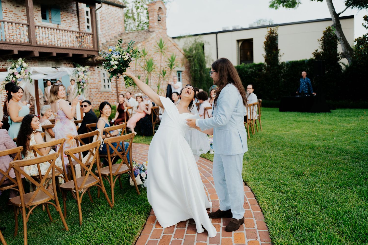 Joyful celebration during an outdoor wedding ceremony with wooden chairs and brick pathway.