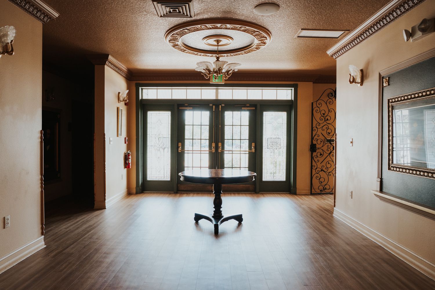 Modern empty room with wooden floors, ornate ceiling fixture, and large glass doors.