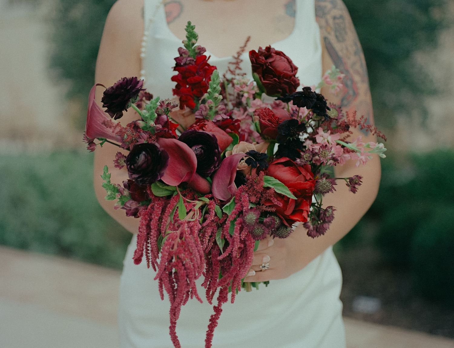 Bride holding dramatic dark red and burgundy wedding bouquet with calla lilies and roses with tattoos.