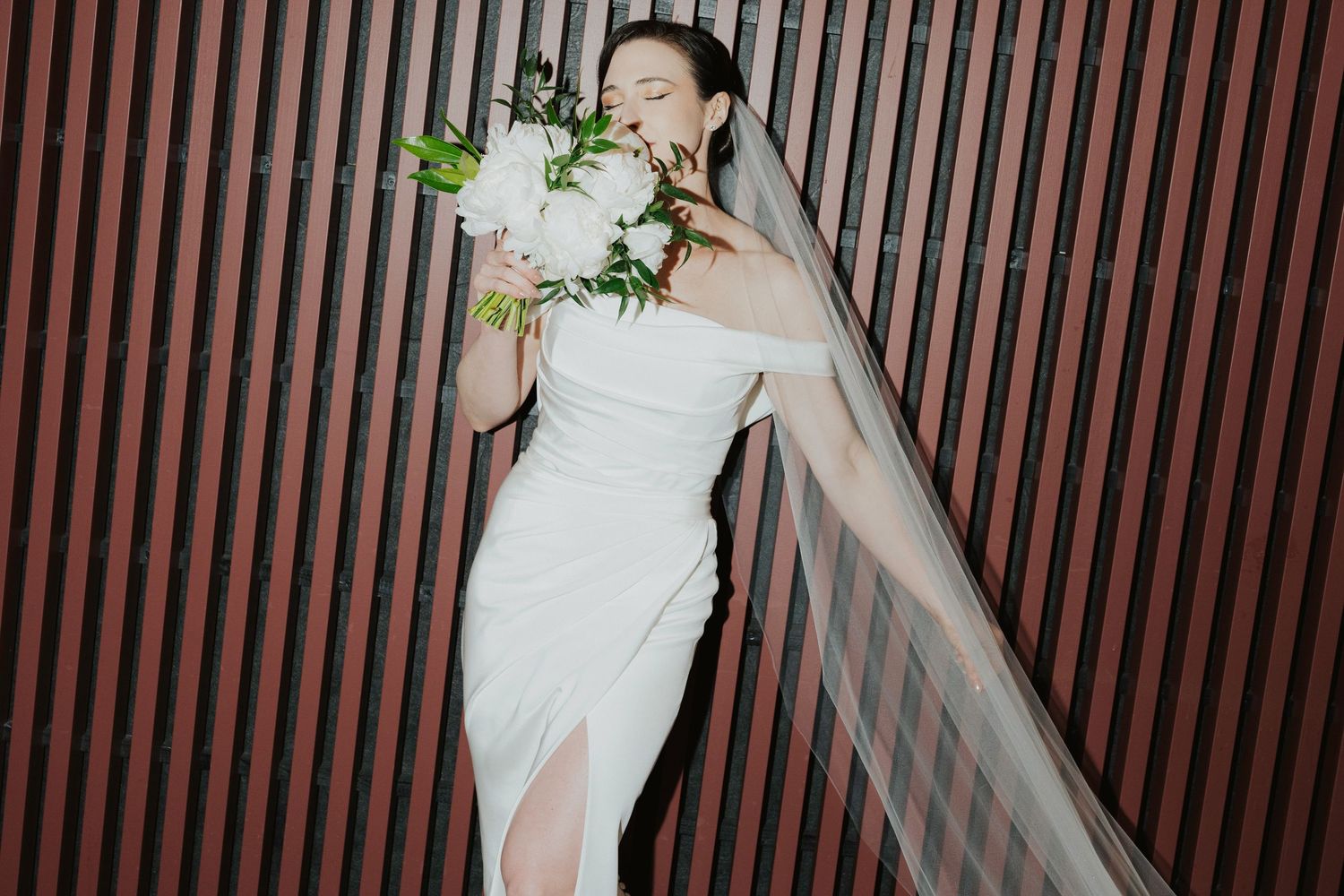 Elegant wedding ceremony with guests gathered in a modern venue featuring vertical wood paneling and soft lighting.