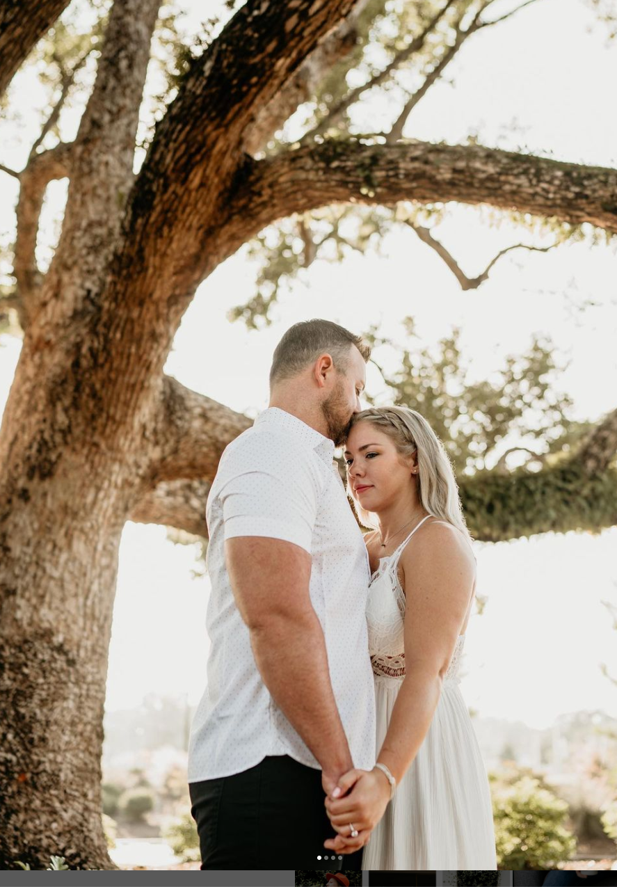 Romantic portrait of a couple embracing under a large oak tree.
