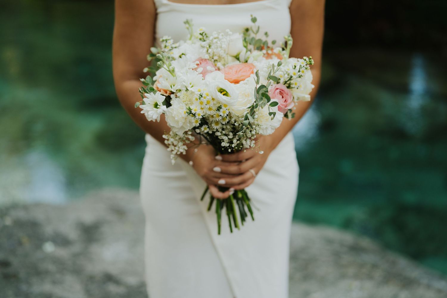 A delicate bridal bouquet with pink and white flowers held against a white dress.