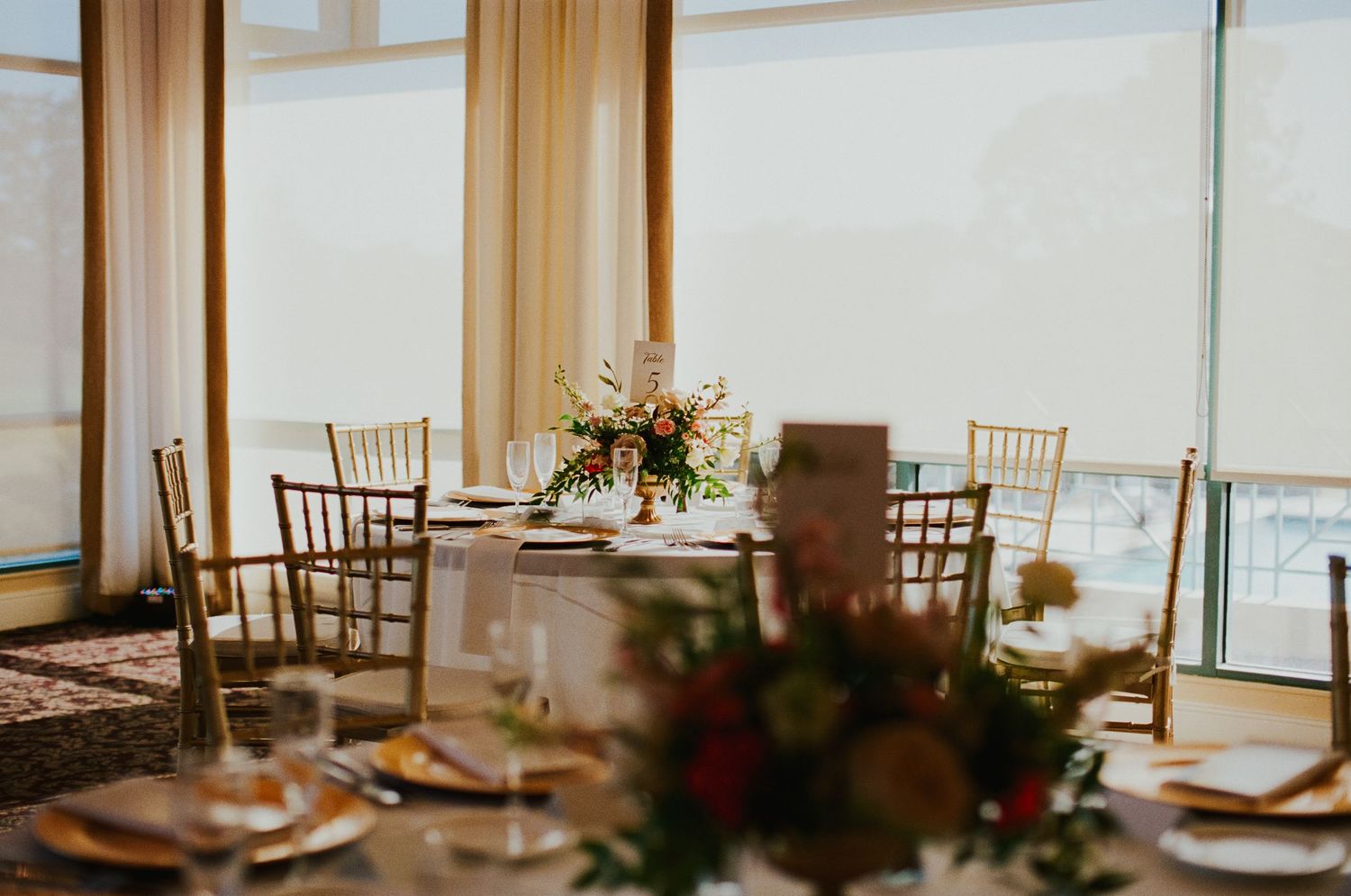 Elegant wedding reception venue with gold chiavari chairs, floral centerpieces, and floor-to-ceiling windows.