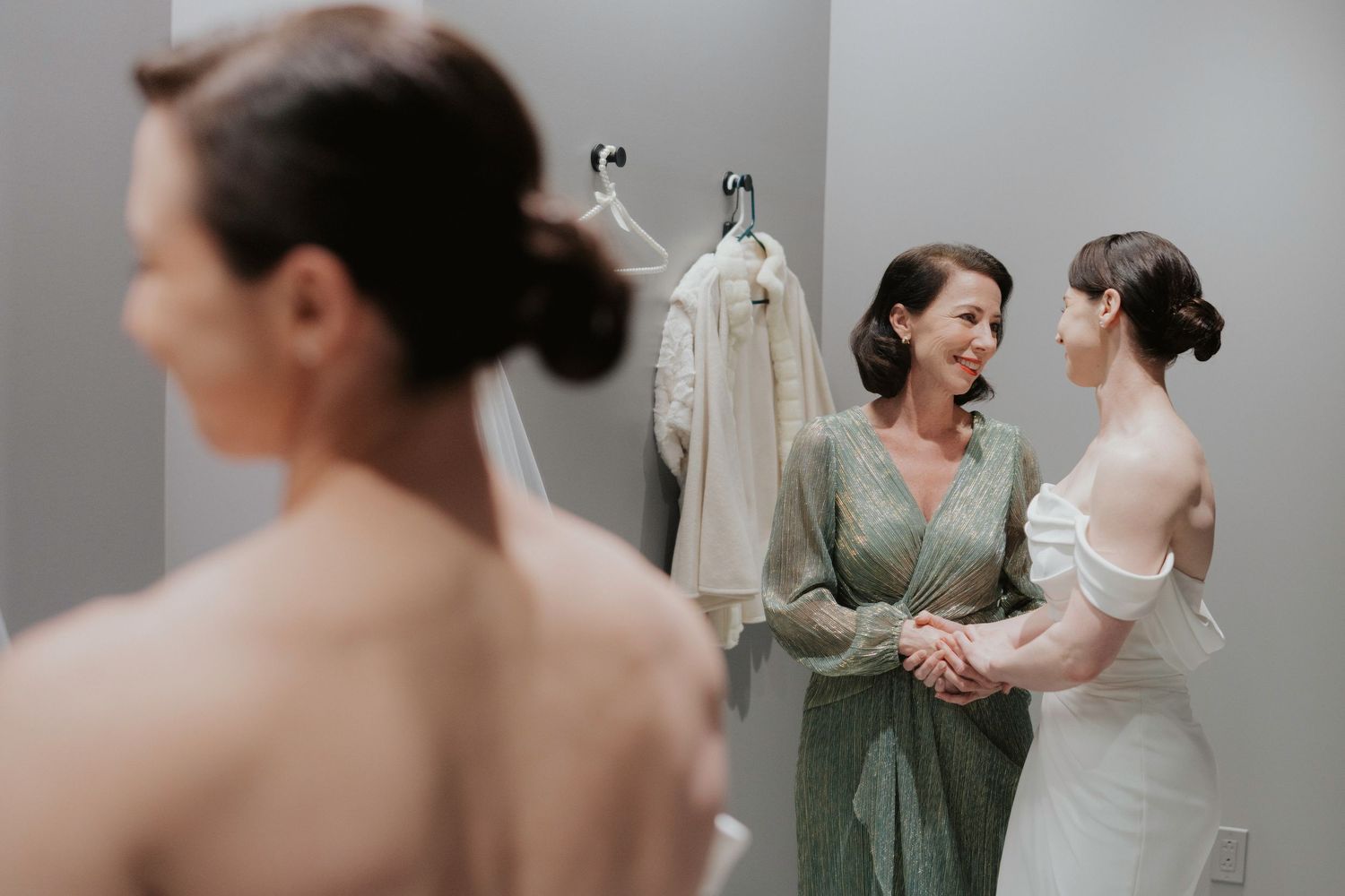 Wedding party members help the bride get ready in a soft-lit dressing room.