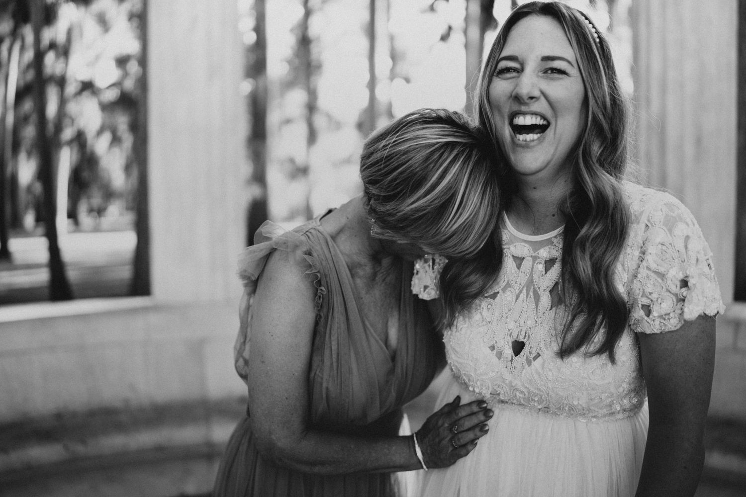 Two friends sharing a candid joyful moment outdoors in black and white photography.