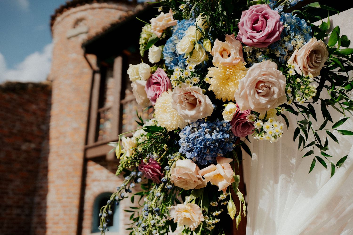 Elegant floral wedding arrangements featuring pink roses and blue hydrangeas against a brick backdrop.