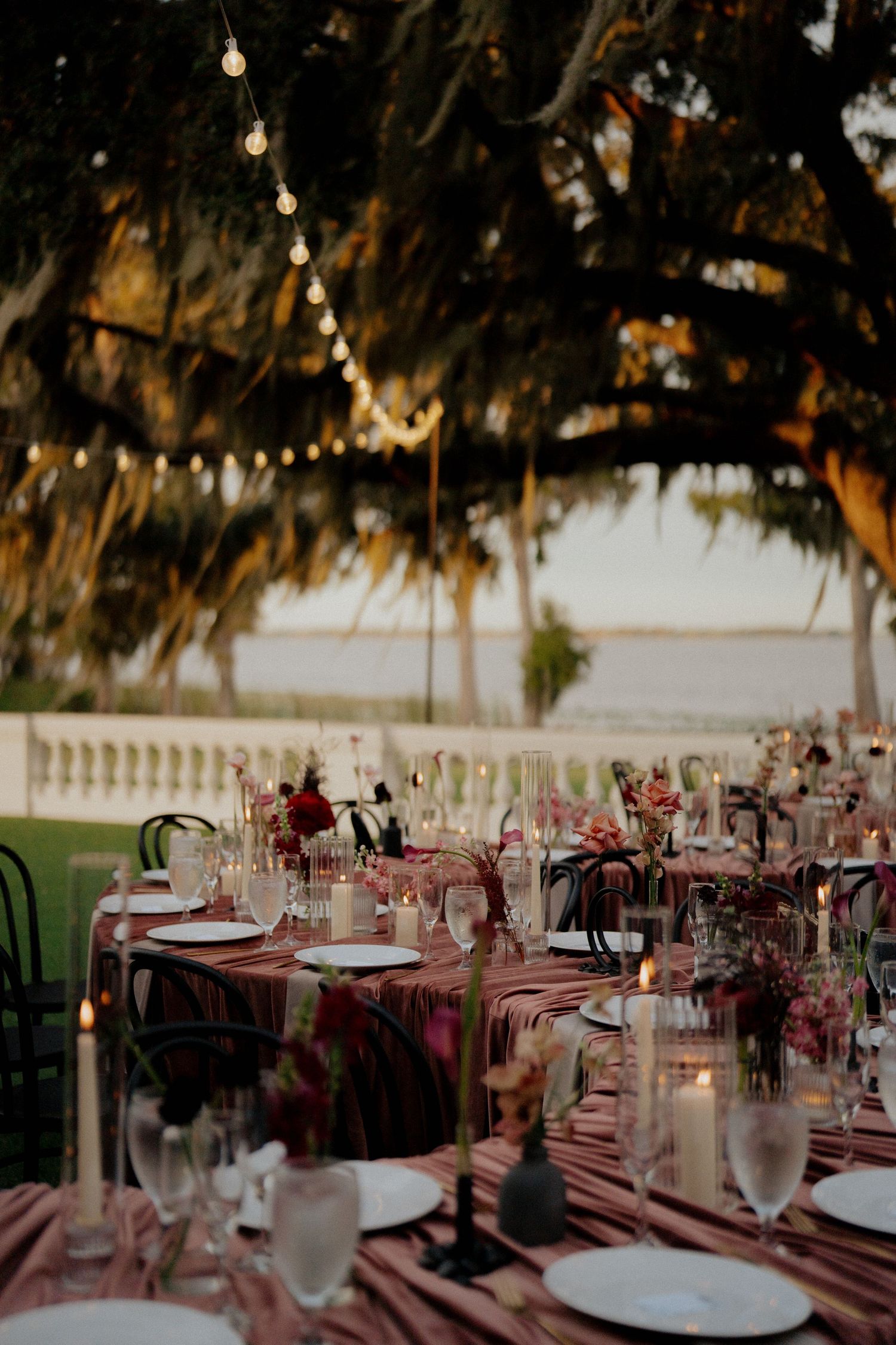 Elegant outdoor wedding reception tables with pink linens, candles, and floral centerpieces under Spanish moss trees.