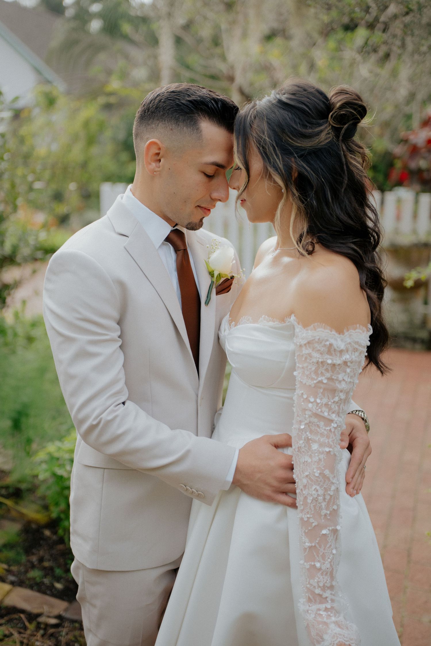 A romantic wedding couple in white attire share intimate moments in a garden setting.