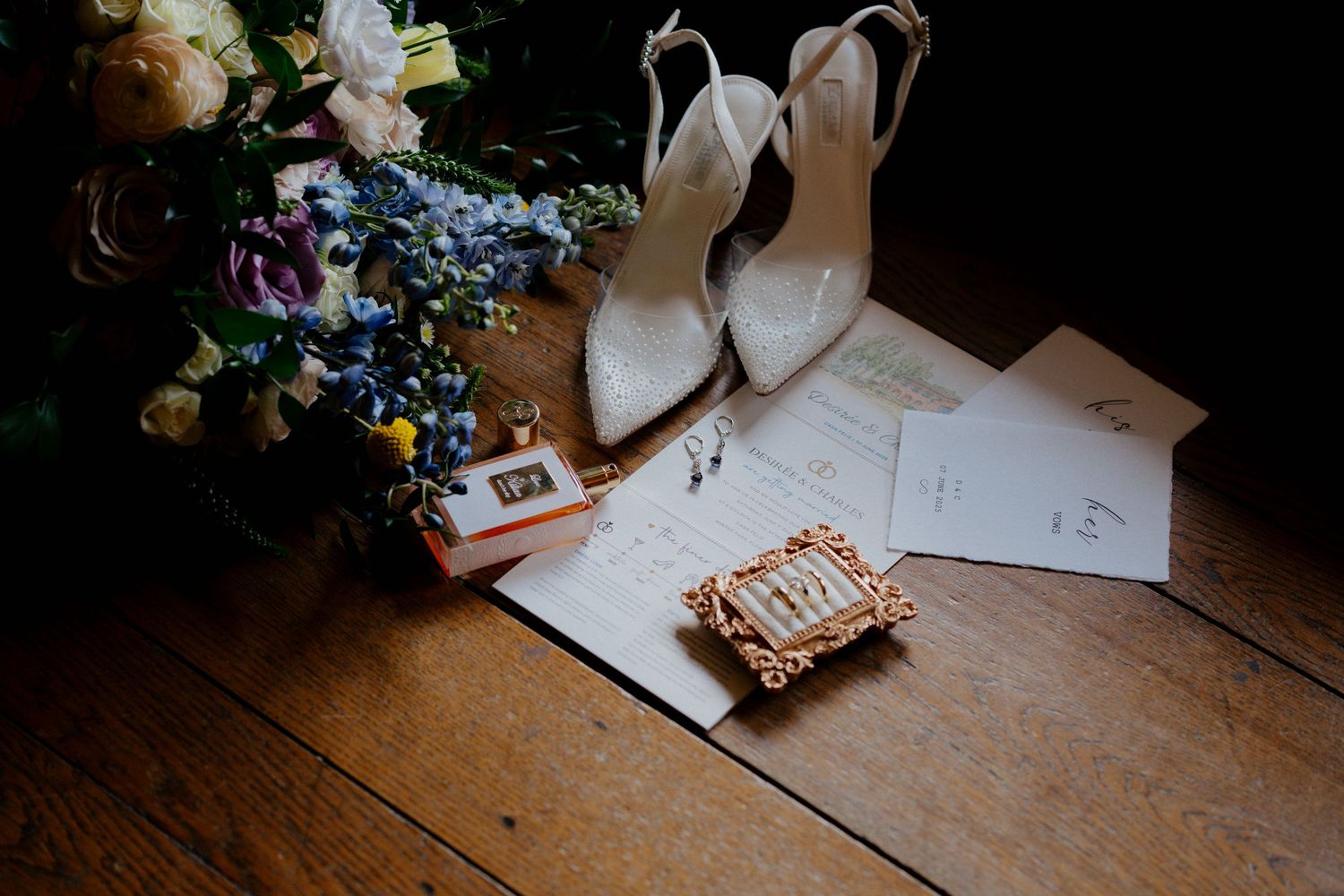 Writing supplies and floral arrangements sit on a rustic wooden table during a wedding preparation.