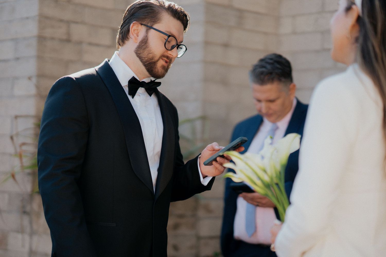 A couple exchanging vows during an intimate outdoor wedding ceremony with a person officiating in the background.