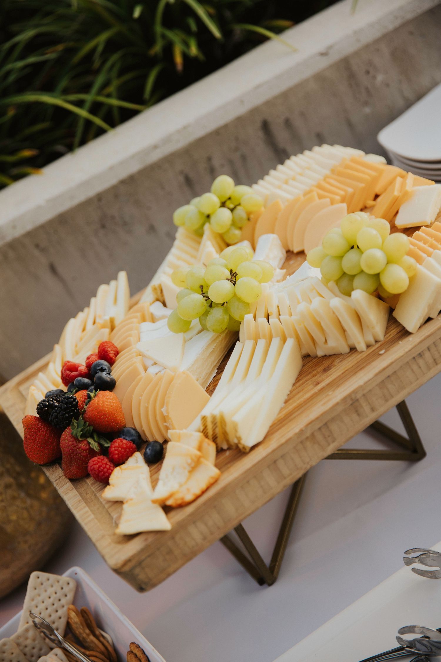 Wooden charcuterie board with sliced cheeses, fresh grapes, berries and fruit arranged elegantly for entertaining.
