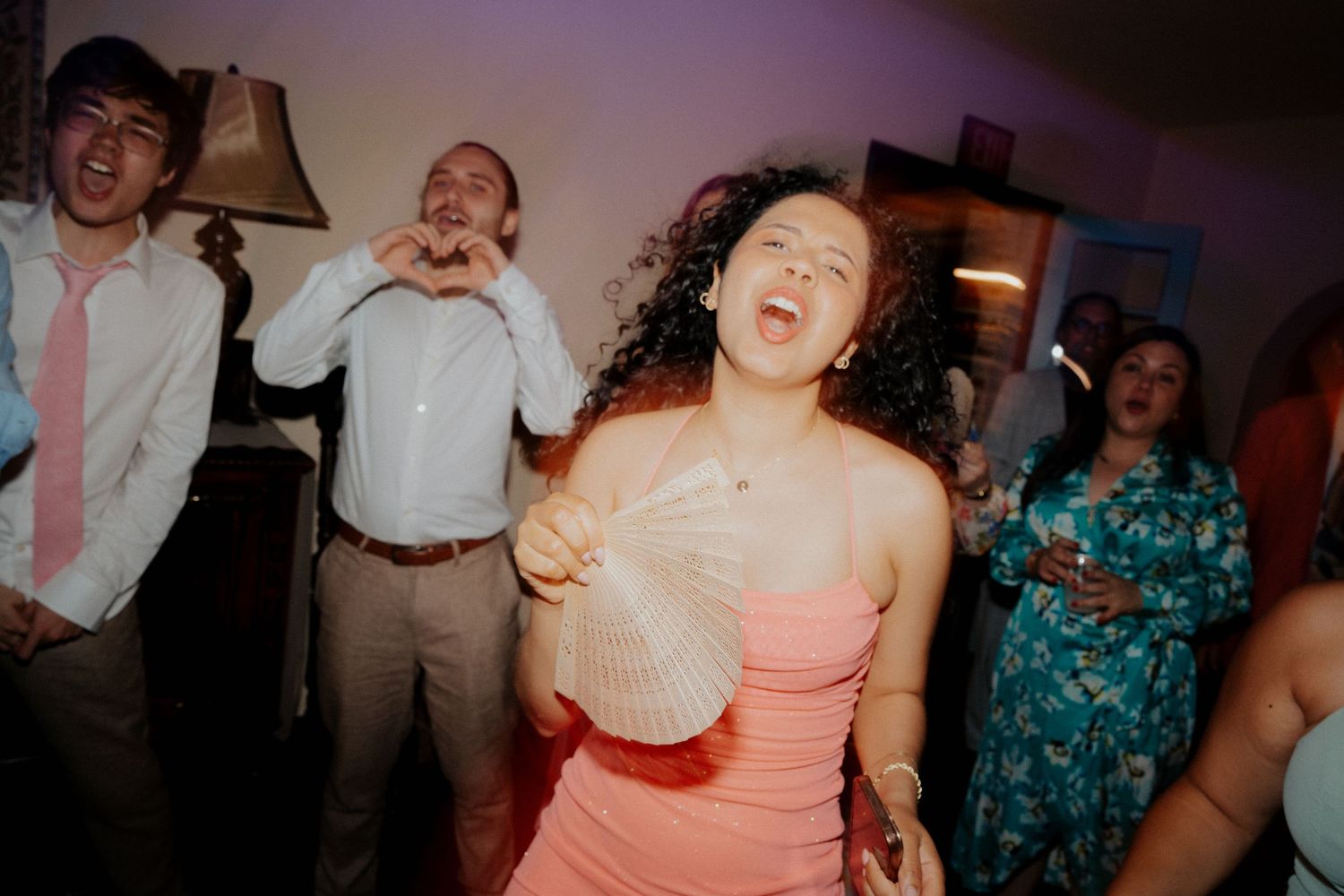 Joyful wedding party guests dancing and laughing together at an indoor reception venue.