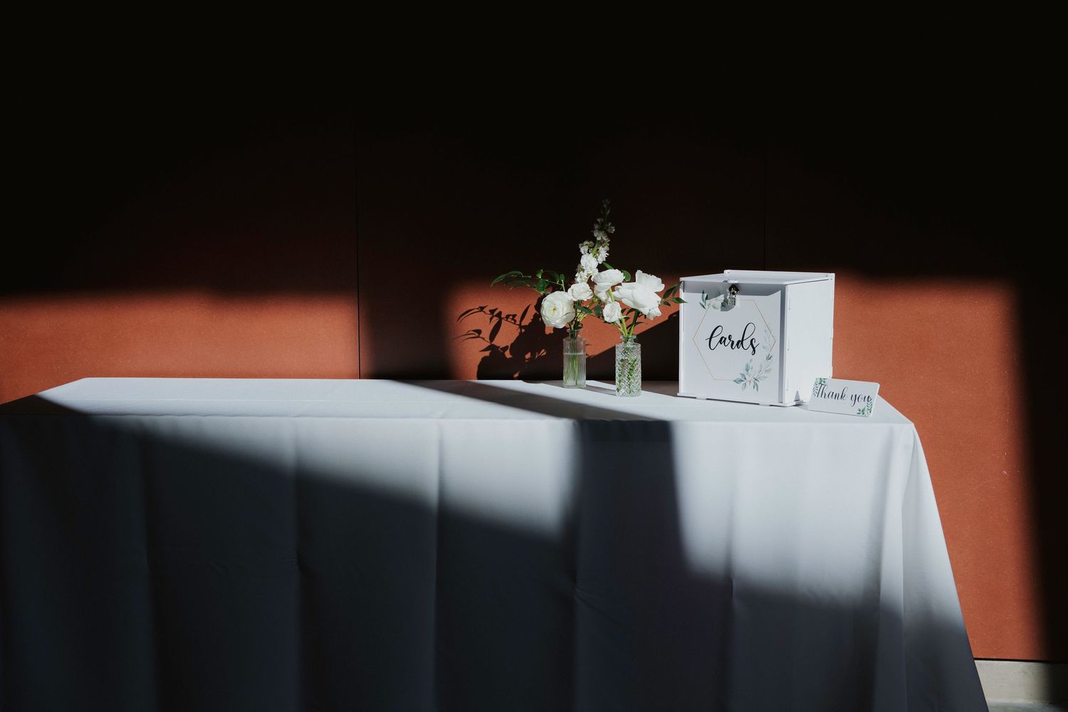 A minimalist wedding reception table setup with cards and decor casting dramatic shadows against an orange wall.