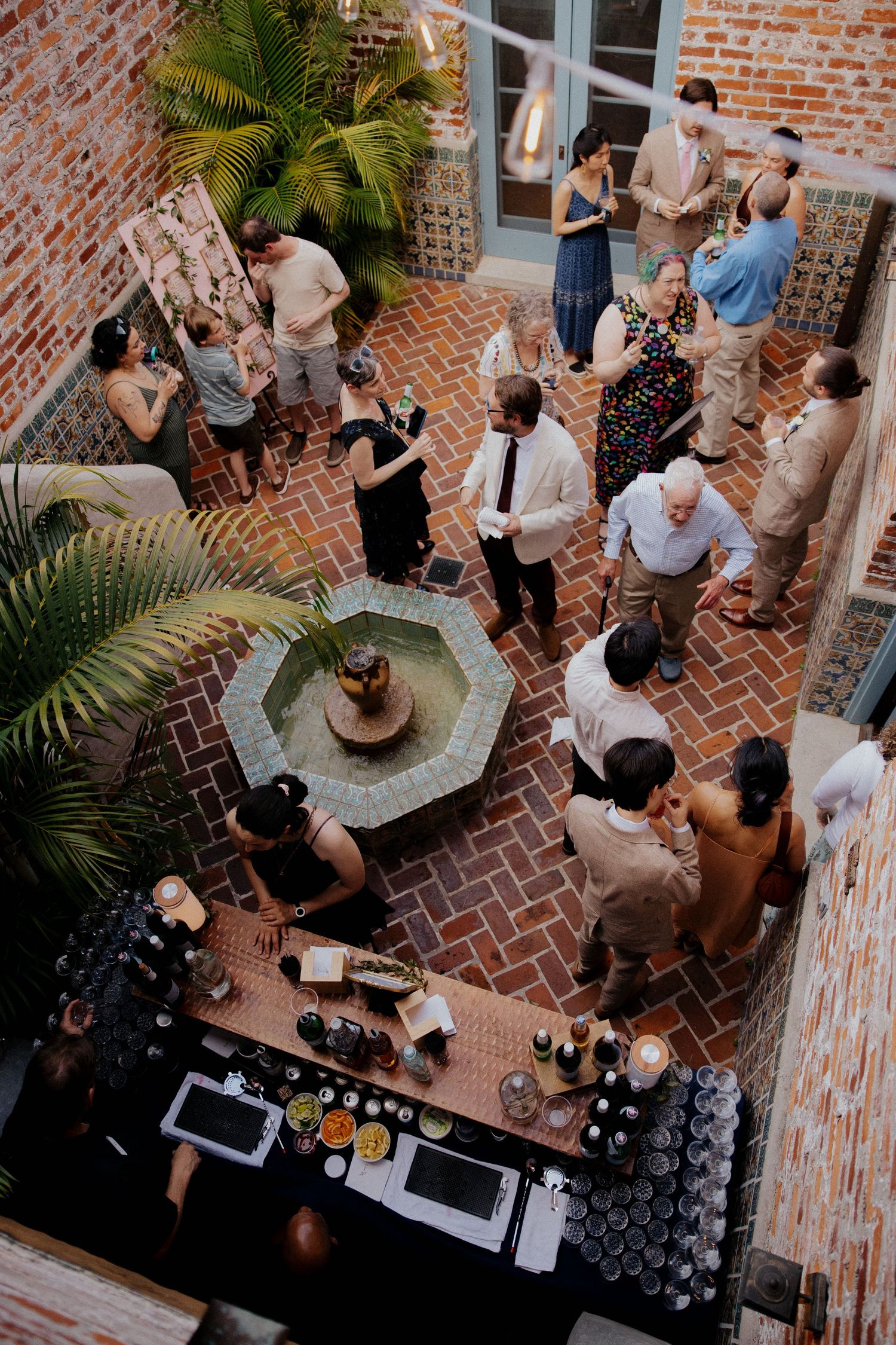 Aerial view of wedding reception courtyard with brick patio, bar setup and mingling guests.