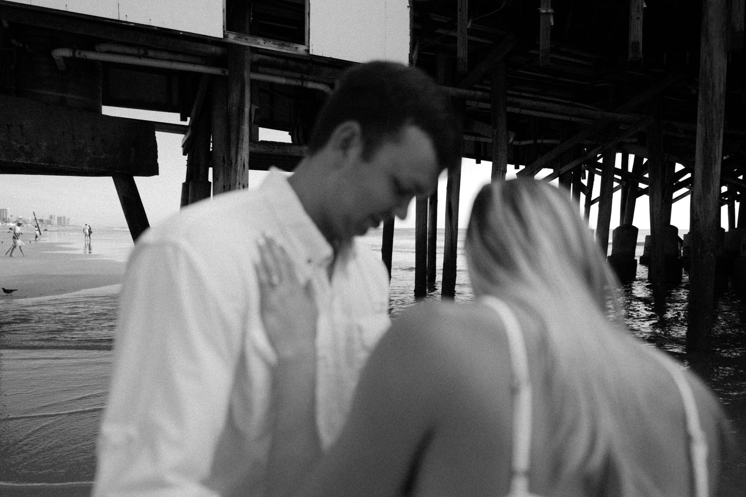 An intimate black and white moment shared under a wooden pier structure.