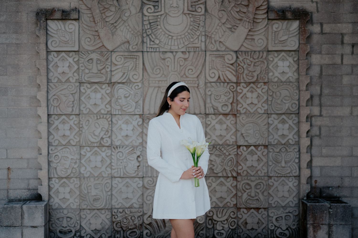 Person in white outfit poses against a stone wall with carved decorative details.