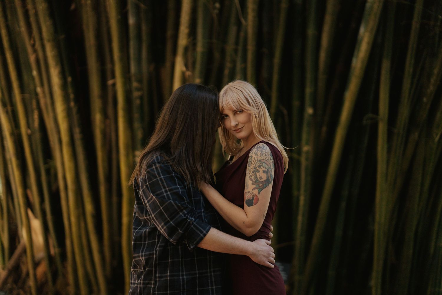 Two people embracing intimately among tall bamboo stalks in atmospheric lighting.